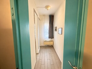 A hallway with teal walls, a ceiling light, a radiator, and a window with curtains. - Antica Corte Di Pisa Near Train Station (Pisa)
