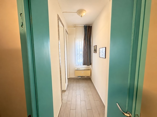 A hallway with teal walls, a ceiling light, a radiator, and a window with curtains. - Antica Corte Di Pisa Near Train Station (Pisa)