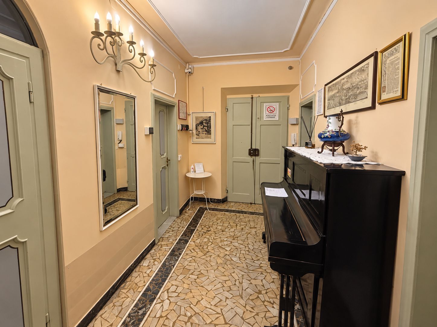 A hallway with a piano, a small table with a vase, and framed pictures on the wall.