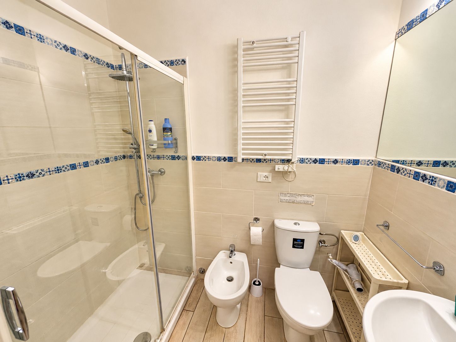A bathroom with a glass-enclosed shower, a toilet, bidet, and a sink.