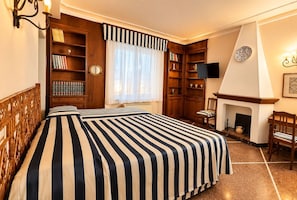 A hotel room with a large bed, a fireplace, a bookshelf, and a television. - Antica Corte Di Pisa Near Train Station (Pisa)