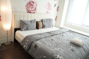 Une chambre à coucher avec un lit, une lampe de chevet, une fenêtre et des motifs floraux décorant le mur.