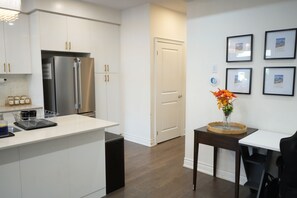 Una cocina moderna con armarios blancos, un refrigerador de acero inoxidable y un comedor con una pequeña mesa y sillas.