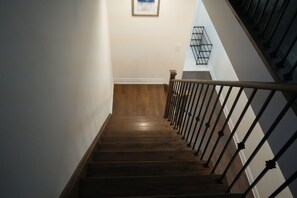 Una escalera de madera con barandilla de metal, que lleva a un rellano con una lámpara fijada a la pared.