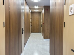 Un pasillo con puertas de madera, placas con números de habitaciones y piso de baldosas.