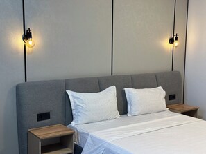 Un dormitorio moderno con un cabecero tapizado gris, dos mesitas de noche y una cama con ropa blanca de cama.