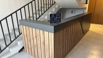 Un mostrador de recepción con detalles de madera y una superficie gris, situado cerca de una escalera con barandilla negra.