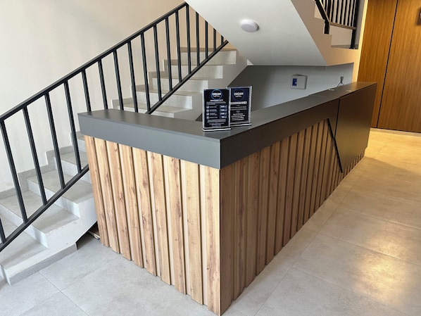 A reception desk with a wooden finish and a grey top, located near a staircase with a black railing.