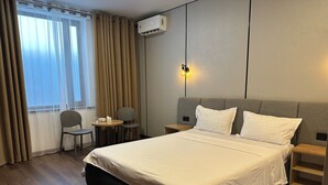 A hotel room with a large bed, a bedside table, a chair, a small table with a lamp, and a window with curtains. - Dream Jaiylgan (Bishkek)