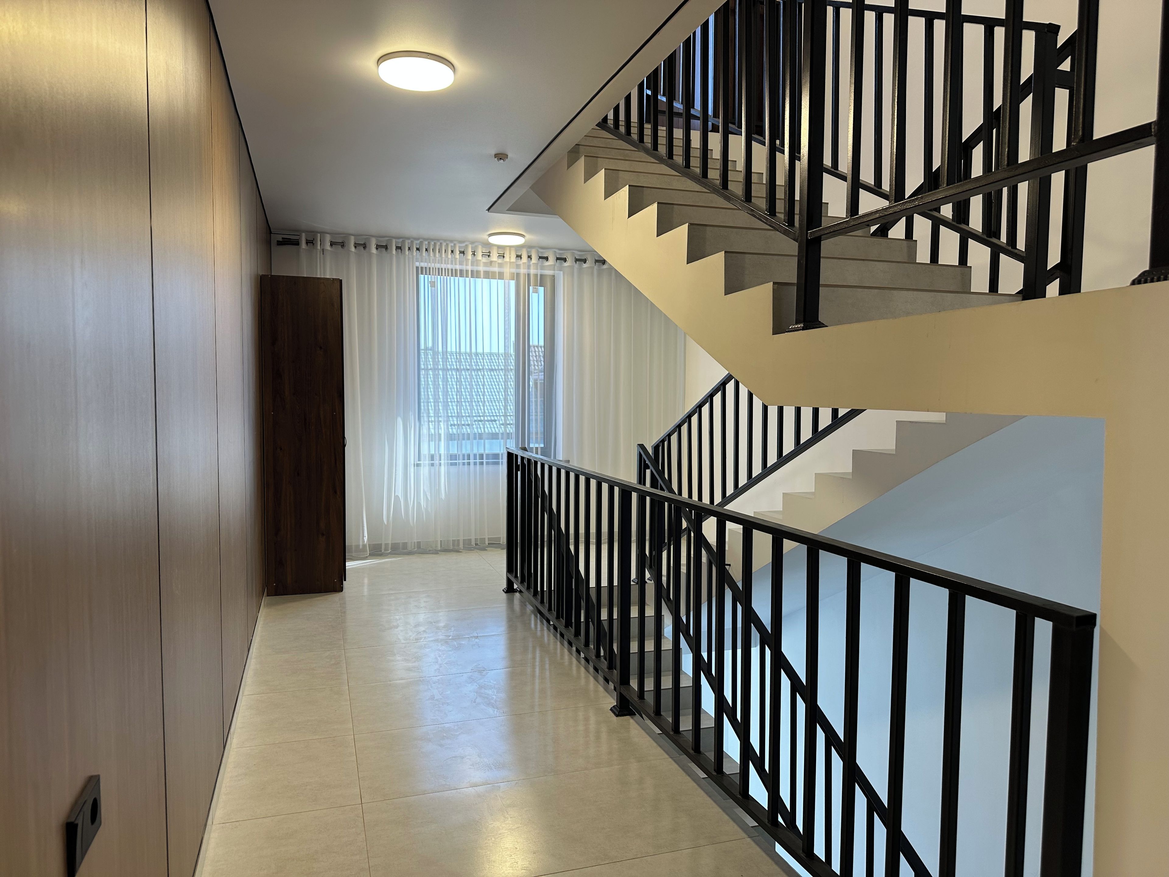 Un interno moderno con una scala, una porta in legno e una finestra con tende leggere.