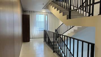 Un interno moderno con una scala, una porta in legno e una finestra con tende leggere.