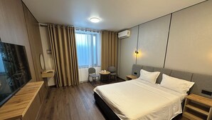 A hotel room with a bed, a desk, a chair, a TV, and a window with curtains. - Dream Jaiylgan (Bishkek)
