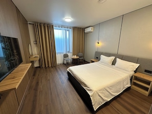 Hotellihuone, jossa on sänky, työpöytä, tuoli, televisio ja ikkuna, jossa on verhot.