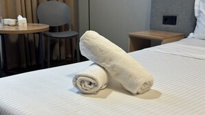 A neatly made bed with two rolled towels and a small table with a cup and tissue box. - Dream Jaiylgan (Bishkek)