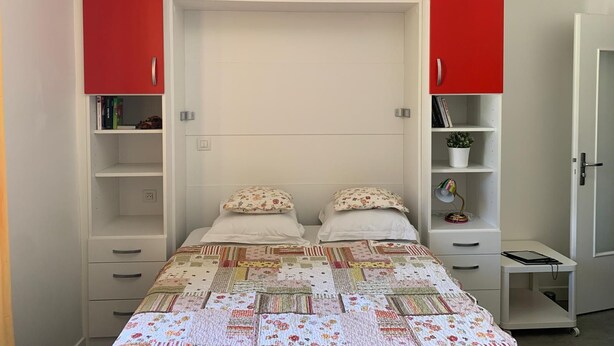 Un dormitorio con una cama, dos mesitas de noche, un armario con puertas rojas y un escritorio pequeño con una silla.