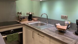 Una cocina moderna con campana de acero inoxidable, horno integrado, un lavamanos con grifo y una encimera con diversos utensilios de cocina.
