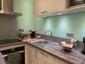 Una cocina moderna con campana de acero inoxidable, horno integrado, un lavamanos con grifo y una encimera con diversos utensilios de cocina.