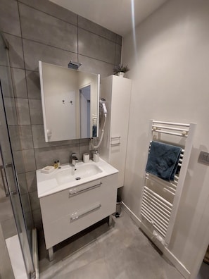 Une salle de bain moderne avec un meuble-lavabo blanc, un miroir, un porte-serviettes et une douche.