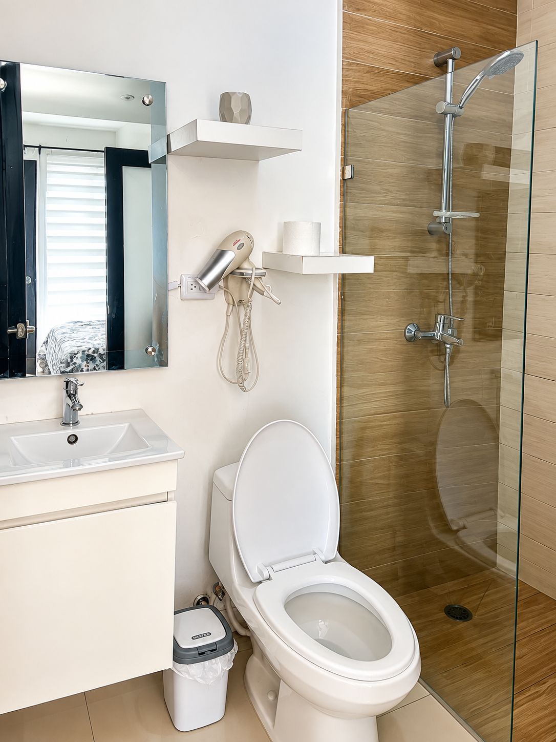 Een moderne badkamer met een douchecabine van glas, een wit toilet, een wastafel en een haardroger bevestigd aan de muur.