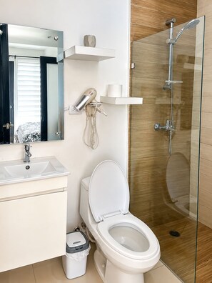 Ein modernes Badezimmer mit Duschkabine aus Glas, einer weißen Toilette, einem Waschbecken und einem an der Wand befestigten Föhn.