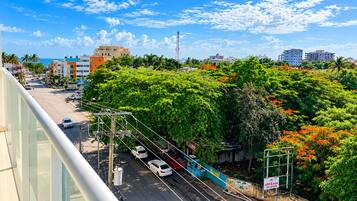 A cityscape with a clear sky, a street with parked cars, and a dense green area with trees.