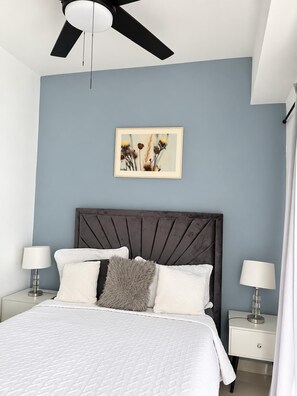 Ein Schlafzimmer mit einem Bett, zwei Nachttischen, einem Deckenventilator und einem an der Wand hängenden Bild.
