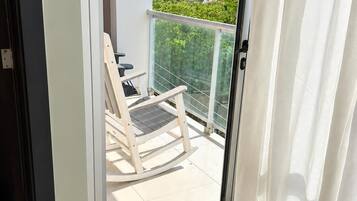 A balcony with a white chair and a glass door leading to an outdoor area.