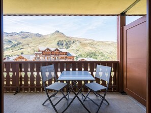 Un balcó amb una taula i dues cadires, amb vista a un paisatge muntanyós i un edifici de fusta.