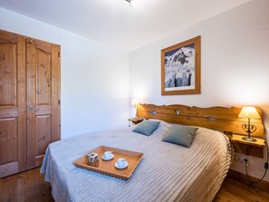A bedroom with a wooden headboard, a bed with a striped blanket, a tray with tea set, and a framed picture on the wall. - Bright apartment near slopes - 6 guests (Les Menuires)