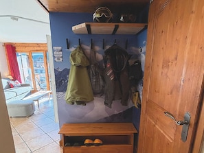 Ett rum med en dörr av trä, en klädställning med jackor, en bänk med skor och ett fönster med utsikt över bergen.