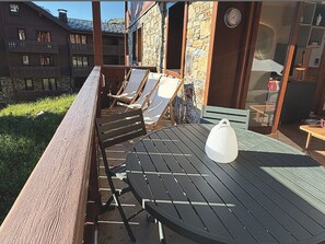 A patio with a table and chairs, a stone wall, and a wooden building in the background. - Bright apartment near the slopes (Les Menuires)