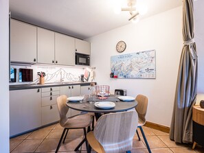 A compact kitchen with a dining area, a clock, and a map on the wall. - Bright apartment near the slopes (Les Menuires)