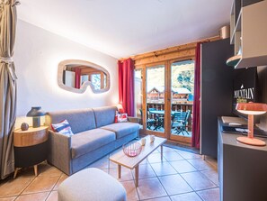 Un salon moderne avec un canapé, une table basse et une vue sur une station de montagne, visible à travers des portes vitrées.