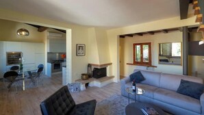 A modern living room with a sofa, a glass coffee table, and a fireplace. There is a dining area with a glass table and chairs, and a kitchen in the background. - FLORENCE DUPLEX RETREAT WITH ICONIC DUOMO & BELL TOWER VIEWS (Firenze)