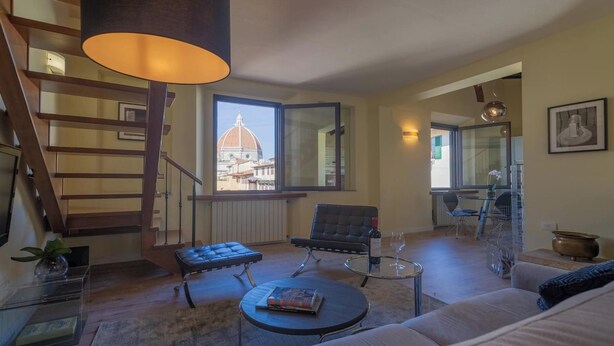 A living room with a staircase, a view of a dome, a sofa, a coffee table, and a chair. - FLORENCE DUPLEX RETREAT WITH ICONIC DUOMO & BELL TOWER VIEWS (Firenze)