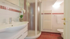 A bathroom with a curved shower enclosure, a sink with a mirror, and a toilet. - FLORENCE DUPLEX RETREAT WITH ICONIC DUOMO & BELL TOWER VIEWS (Firenze)