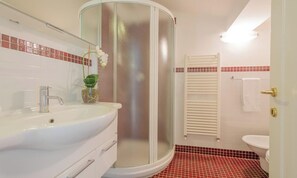 Un baño con cabina de ducha curva, un lavabo con espejo y un inodoro.