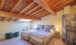 Un dormitorio con dos camas, vigas de madera, un tragaluz, mesitas de noche y una lámpara fijada a la pared.