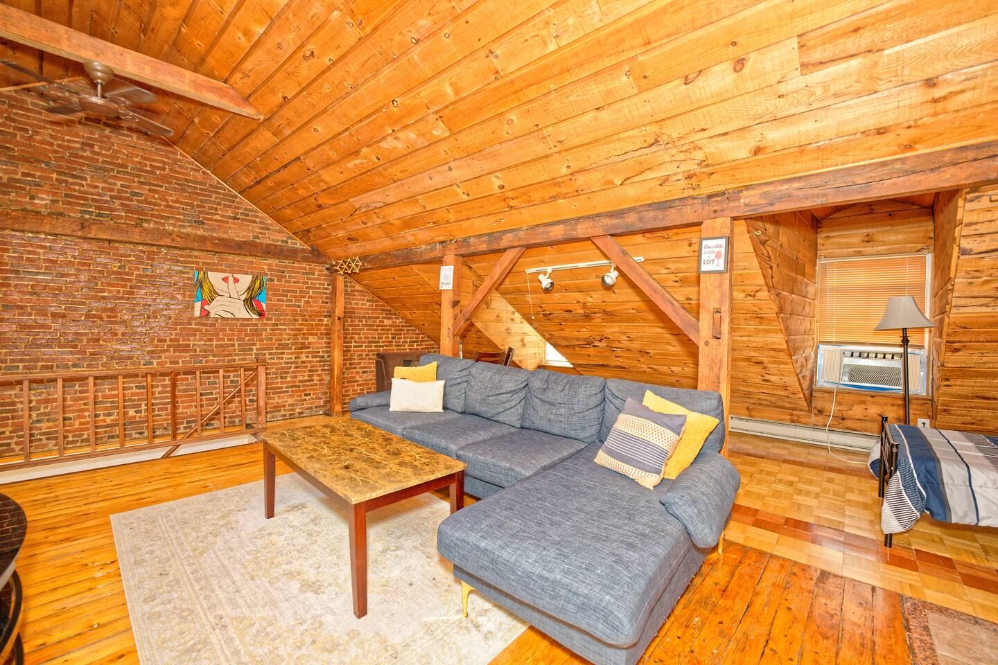 Ein gemütliches Loft mit Backsteinwand, Holzboden und grauem Ecksofa.