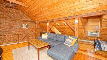 Ein gemütliches Loft mit Backsteinwand, Holzboden und grauem Ecksofa.