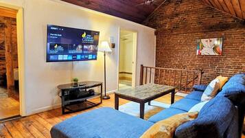 Ein gemütliches Wohnzimmer mit Fernseher, einer Couch, einem Tisch und einer Lampe.