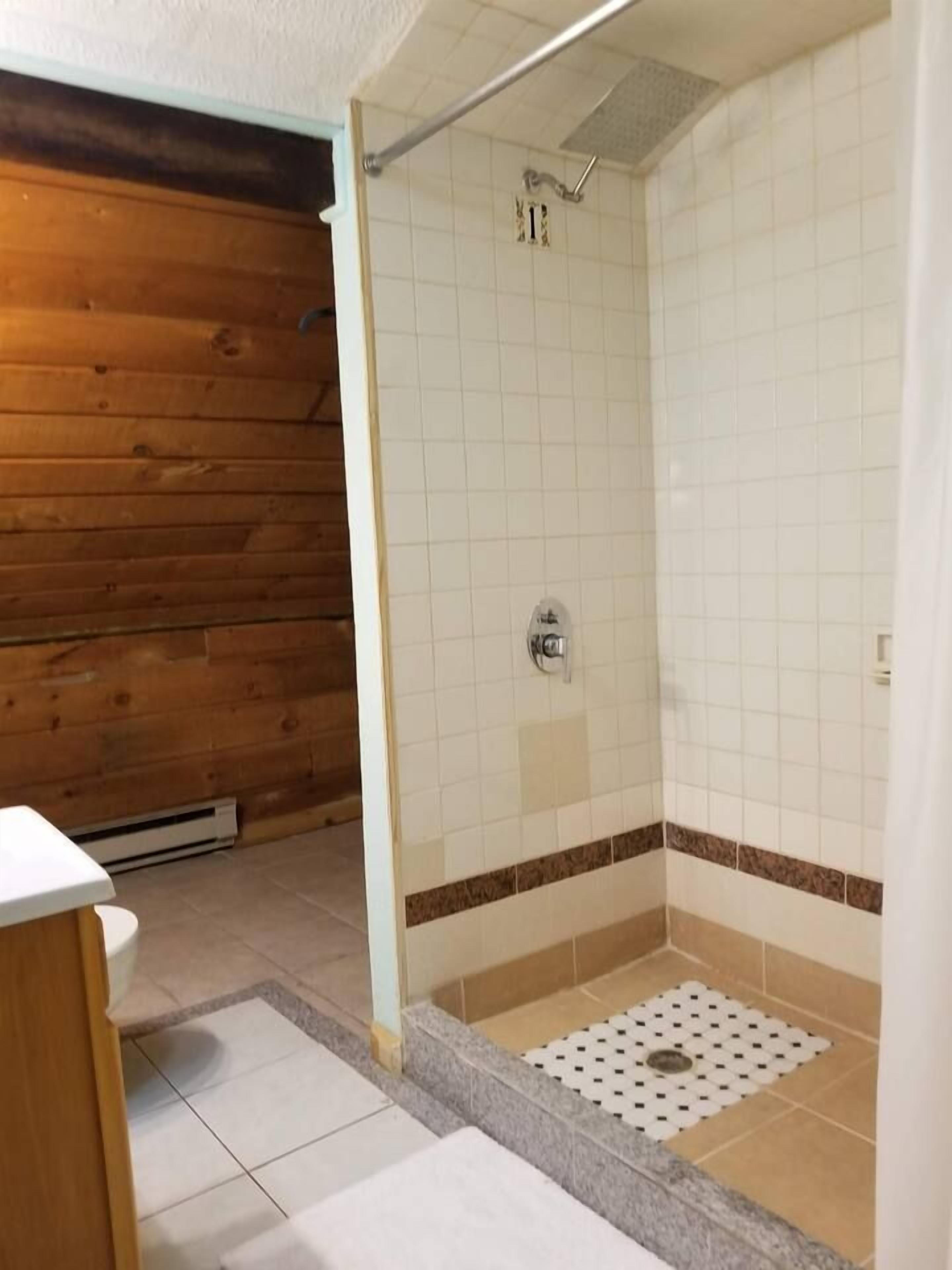 A bathroom with a shower, tiled walls, and a wooden floor.