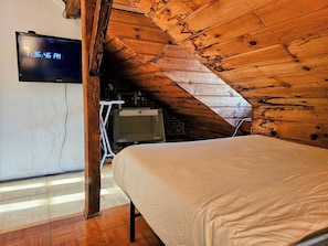 Une chambre à coucher avec un lit, un téléviseur fixé au mur et un plafond en bois.
