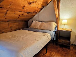 Una cama individual con cabecera en una habitación con paredes de madera y techo inclinado.