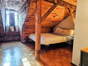 A loft bedroom with a sloped ceiling, wooden beams, a bed, and a window.