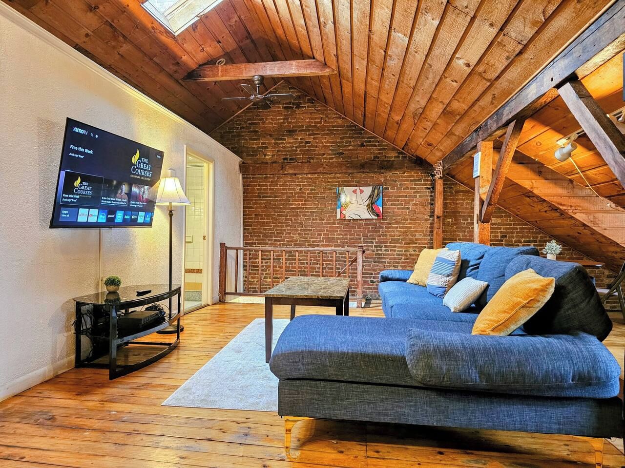 Un salon chaleureux avec un canapé bleu, un téléviseur fixé au mur et un plafond en bois.