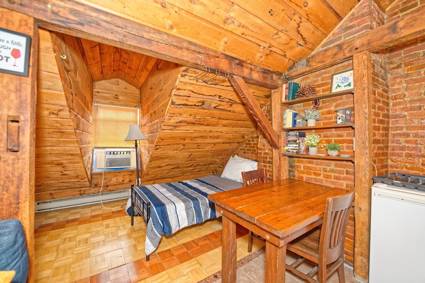 Quarto aconchegante com cama, mesa e parede de tijolos.