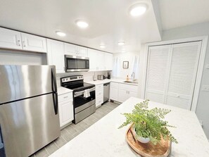 A modern kitchen with stainless steel appliances, white cabinetry, and a central island with a plant.