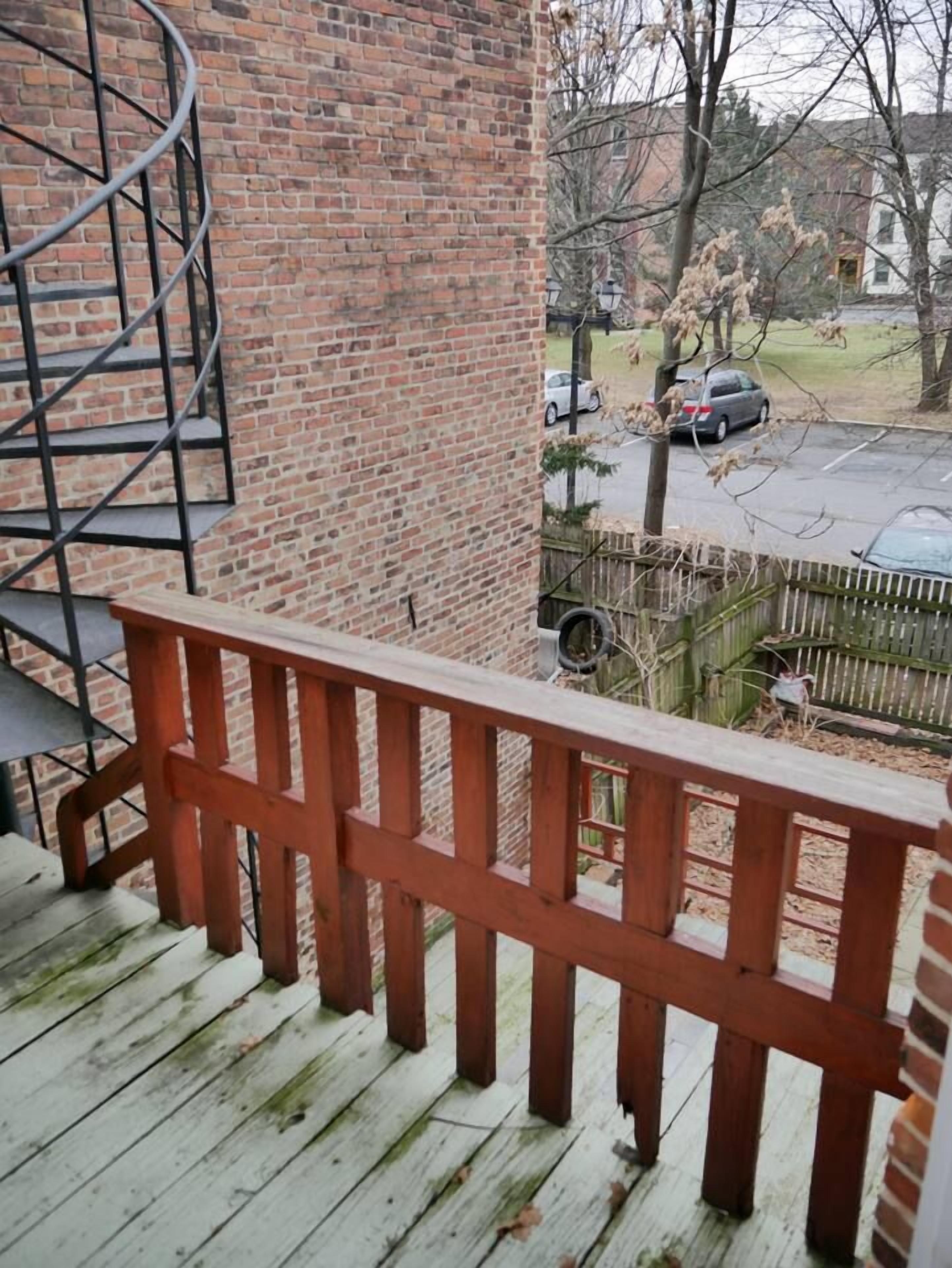 A wooden deck with a metal spiral staircase and a brick wall.