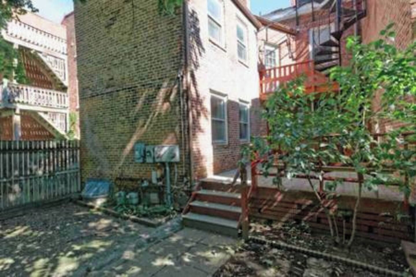 A residential building with a brick facade, a small front yard with steps, and a metal fence.